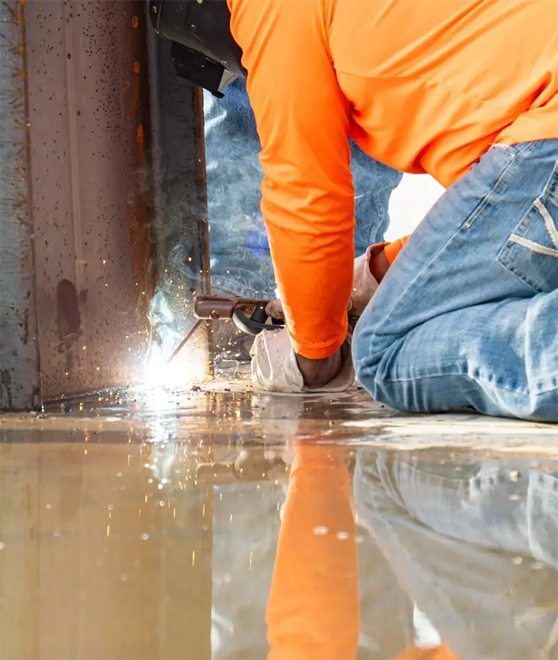 metal solutions welder Worker in an orange shirt kneeling on the ground welding